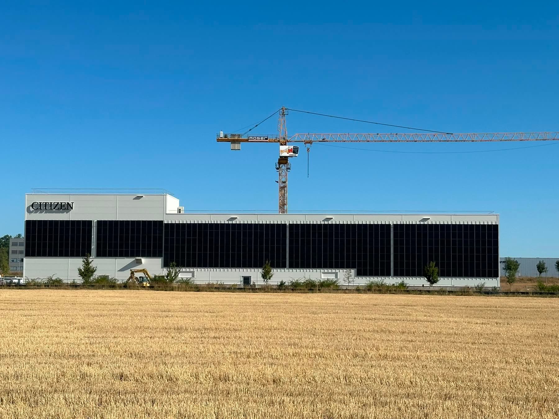 Gewerbehalle, deren komplette Längsfassade mit Solarmodulen belegt ist, davor ein abgeerntetes Feld